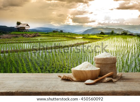 Jasmine rice in bowl and sack on wooden table with the rice field background  - Stock Image - Everypixel