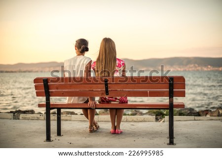 two friends sitting on wood bench near beach on evening sunset