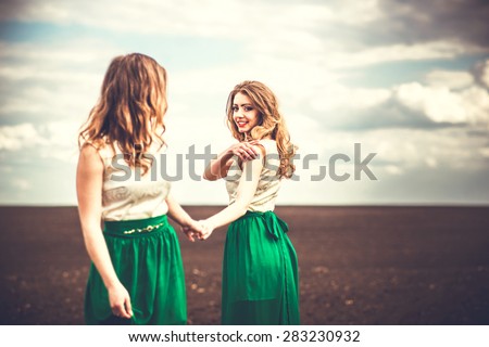 Two pretty girls holding hands in the brown field