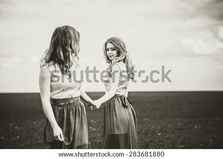 Two pretty girls holding hands in the field, sepia effect