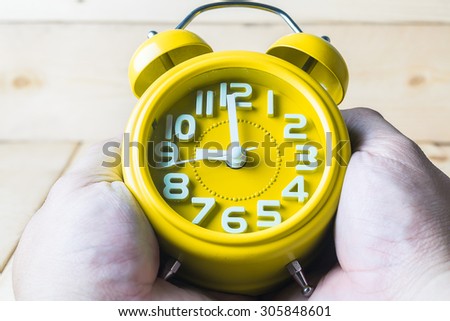 Hand hold Yellow alarm clock on wood background