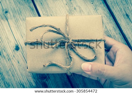 Hands hold A Vintage gift box brown paper wrapped with rope on wood background , vintage tone