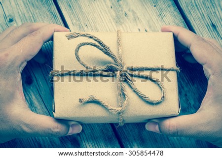 Hands hold A Vintage gift box brown paper wrapped with rope on wood background , vintage tone