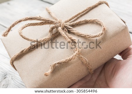 Hands hold A Vintage gift box brown paper wrapped with rope on wood background