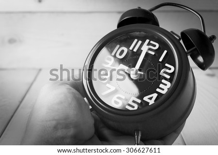 Hand hold alarm clock on wood background , black and white tone