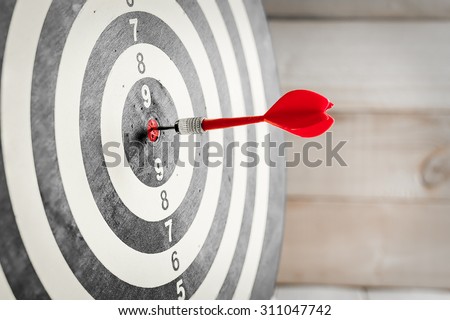 Red dart arrow hitting in the target center of dartboard