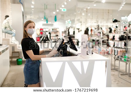 Girl seller in a mask and gloves stands at the checkout in a store. Store seller during COVID-19. Safety during the virus. The seller in the clothing store.