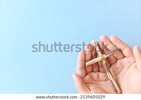 Top view of hand holding wooden cross crucifix with copy space in blue background. Catholicism, Christianity, Thanksgiving, Catholic and Christian faith concept. Stockfoto © 