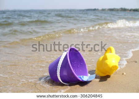 Children\'s toys on the beach on the river bank. Baby bucket, rake and watering can. Waves estuary.