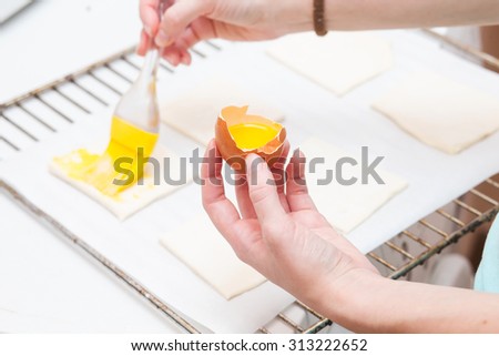 Smearing egg pie. Cooking sweet pastries. Hands