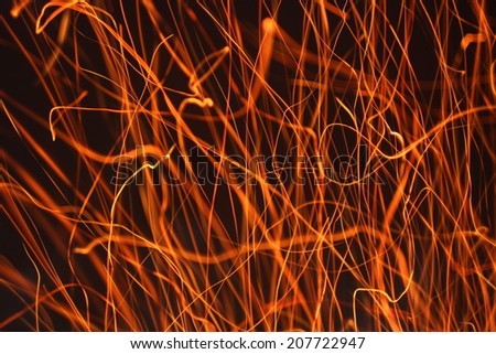 Abstract background with orange traces of hot campfire sparks on dark night blurred field.