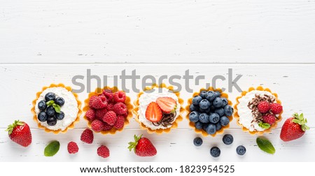 Tartlets (tarts, open pastry pies) with ricotta cheese (cottage cheese) and fresh berries (straberry, raspberry and blueberry). Healthy dessert breakfast, snack, morning table. White wooden background Stok fotoğraf © 