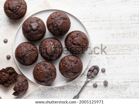 Chocolate muffins on white ceramic plate. Homemade fluffy and moist chocolate cakes. Top view. Copy space. White wooden table background.