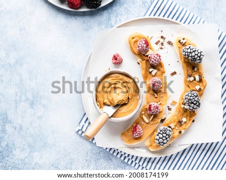 Peanut butter frozen bananas with frozen berries and toppings on ceramic plate. Blue background. Top view. Copy space. Healthy vegetarian dessert, summer refreshing snack or sugar free sweets.