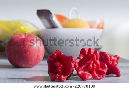 Close view of three red peppers and an apple on the kitchen table./Three red peppers and an apple