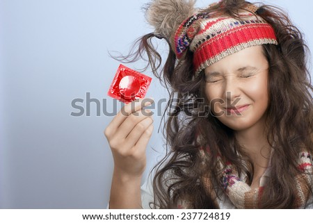 Close view of a girl  with closed eyes, knitted hat and a red condom pack in the hand