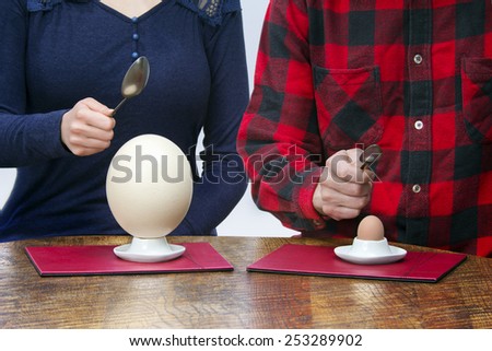 Woman and man with small and big spoons eating hen and ostrich eggs