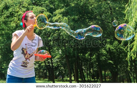 Happy young girl has fun with bubbles in a summer day in a park. She is smiling. She has tattoo and a vintage style with bandana and old school t-shirt
