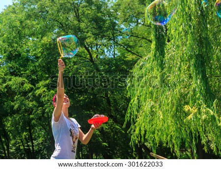 Happy young girl has fun with bubbles in a summer day in a park. She is smiling. She has tattoo and a vintage style with bandana and old school t-shirt