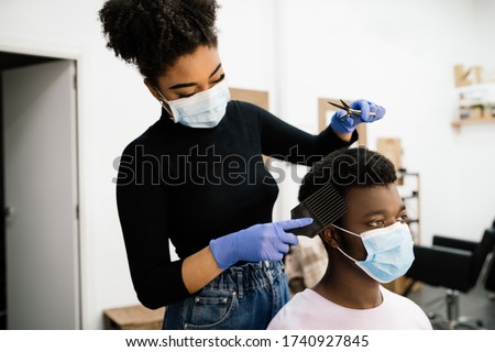 Beauty African-American hairdresser peeling and combing an African-American male client both wearing a face mask and gloves to protect himself from the coronavirus pandemic