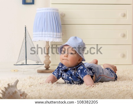 little child baby boy lying on the floor on the carpet indoors in baby room fashion clothing hat