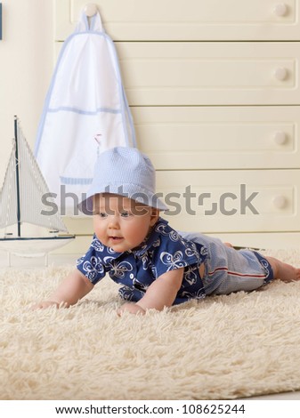 little child baby boy lying on the floor carpet indoors in baby room hat fashion clothing