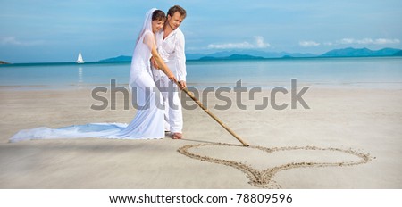 beautiful couple on the beach in wedding dress drawing heart