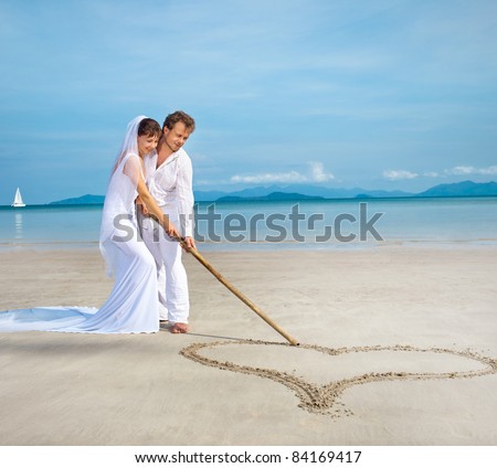 beautiful couple on the beach in wedding dress drawing heart