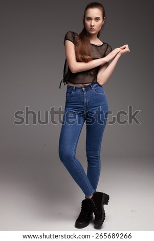 Blond cheerful young woman. Beauty portrait, perfect makeup. Long chic elegant hair. Model tests. Cute girl in black top and jeans. Isolated. Gray background.
