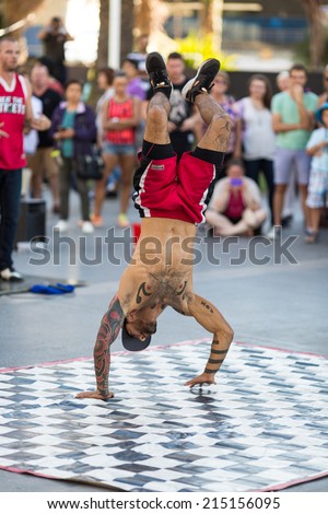 SYDNEY, AUSTRALIA - JUNE 7, 2014: Unknown break-dance street performer spinning on his head in the heart of Darling harbour in front of a crowd of tourists.