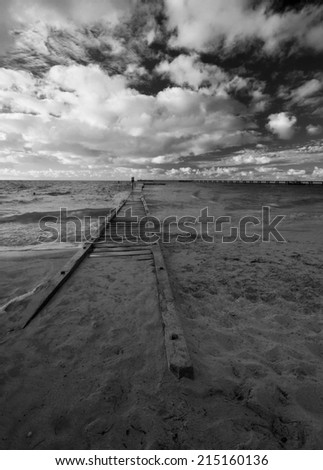 The way to the ocean.  Some sort of a wooden jetty leading straight to the ocean.  Dramatic sky. Black and white.
