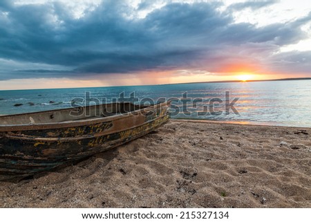 Sunset over the ocean line at the beach with dark clouds and a small fishing boat at the fore ground.