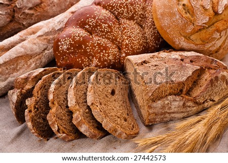 Sliced country-styled brown bread baton and rye spikes on the canvas tablecloth with bread loafs assortment