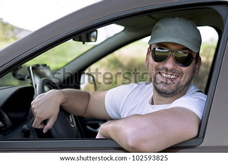 Happy male driver smiling while sitting in a car with open front window. Selective focus.
