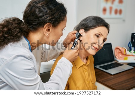 Hearing exam for elderly citizen people. Otolaryngologist doctor checking mature woman's ear using otoscope or auriscope at medical clinic