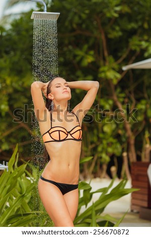 The girl in the shower in the tropics in full growth.Water flows through the body of the girl.Water splashing.