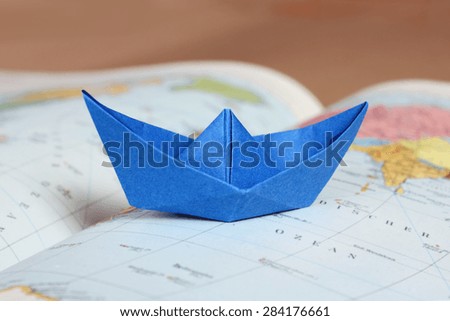Travel planning concept - blue folded paper boat on atlas map with blurred background