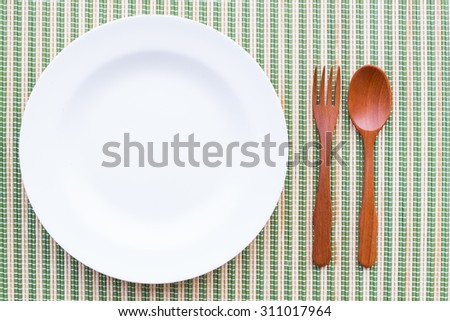 empty white plate and wooden spoon on bamboo mat.