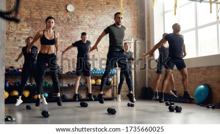 Group of sportive people jumping, warming up before having workout with dumbbells at industrial gym. Group training concept. Horizontal shot Stok fotoğraf © 
