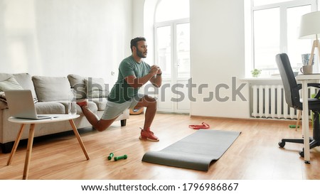 Get Fit At Home. Full length shot of young active man watching online video training on laptop, exercising, stretching during morning workout at home. Sport, healthy lifestyle. Web Banner