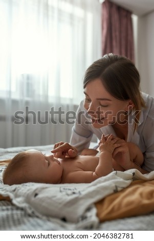 Portrait of happy smiling mother gently touching infant baby's nose, trying to wake him up for feedng. Lovely mother looking at her baby with affection. Modern interior bedroom on backgrond. Foto stock © 
