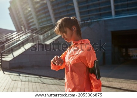 Active millennial woman in sport clothes check time on smartwatch run jog outside follow healthy lifestyle. Toned fit sporty girl in sportswear train workout exercise with smartphone on armband. Foto stock © 