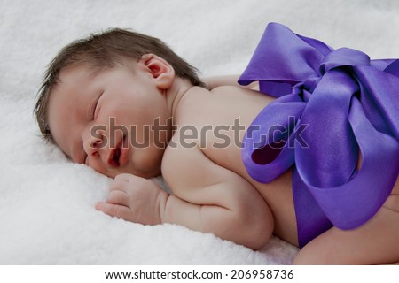 Newborn baby sleep smiling, purple ribbon tied