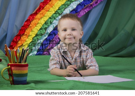 Beautiful baby with blue eyes drawing pencils on the background of bright rainbow