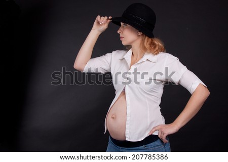 Portrait of pregnant woman in white shirt and black hat, black background