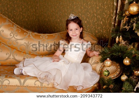 Beautiful girl in the princess finery near the Christmas tree, golden hues. Christmas, New Year