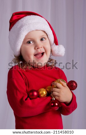 Joyful baby with Christmas toys in Santa\'s hat. Getting ready to decorate a Christmas tree. Christmas, New Year