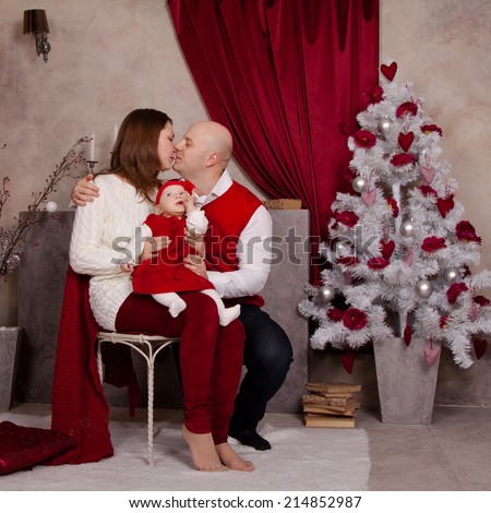 Happy family in santa hat near Christmas tree. Dad hugging and kissing his mother, waiting Christmas miracle, New Year