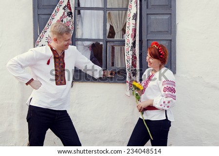 Loving couple in the Ukrainian national clothes near a window farmhouse. Open-air museum Pirogovo, Kyiv, Ukraine