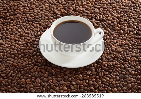 White cup of black coffee standing on roasted coffee beans. AÂ�ll in focus.